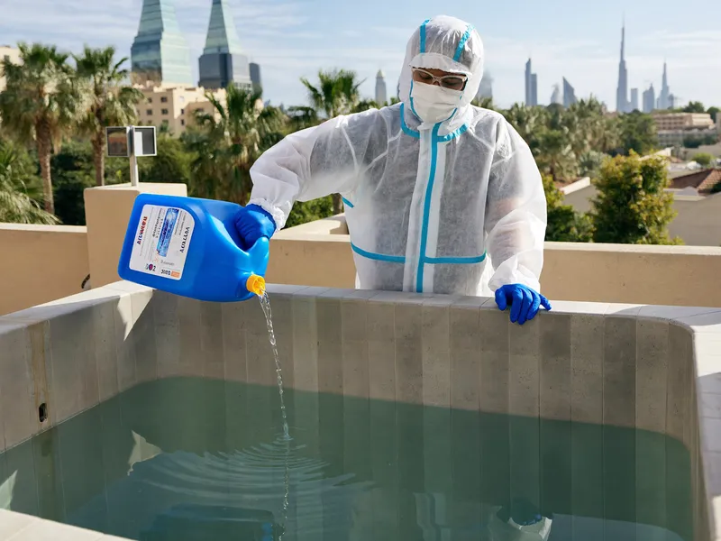 Technician dosing disinfectant into a clean empty water tank with a measuring container
